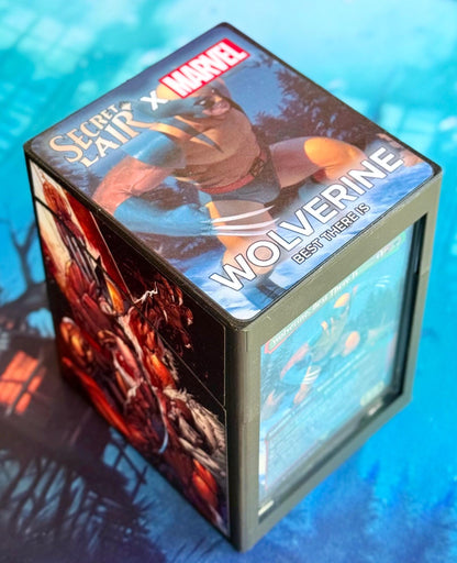 May include: A black card box with a Secret Lair x Marvel Wolverine design. The box has a blue and yellow image of Wolverine on the top and a red and black image of Wolverine on the side. The text on the box reads 'Secret Lair x Marvel' and 'Wolverine Best There Is.'
