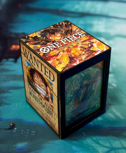 May include: A black card game box with a One Piece Card Game logo. The box has a wanted poster on one side with a cartoon image of Monkey D. Luffy and the text 'WANTED DEAD OR ALIVE MONKEY-D-LUFFY MARINE.' The other side of the box has a colorful image of a character from the One Piece anime. The box has a clear plastic window on one side to show the cards inside.